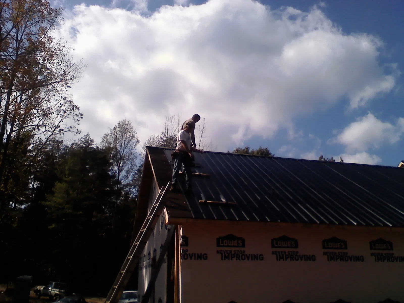 Roofer fastening dark metal panels high against a cloudy sky, from a Roof Inspection job in Port Hueneme