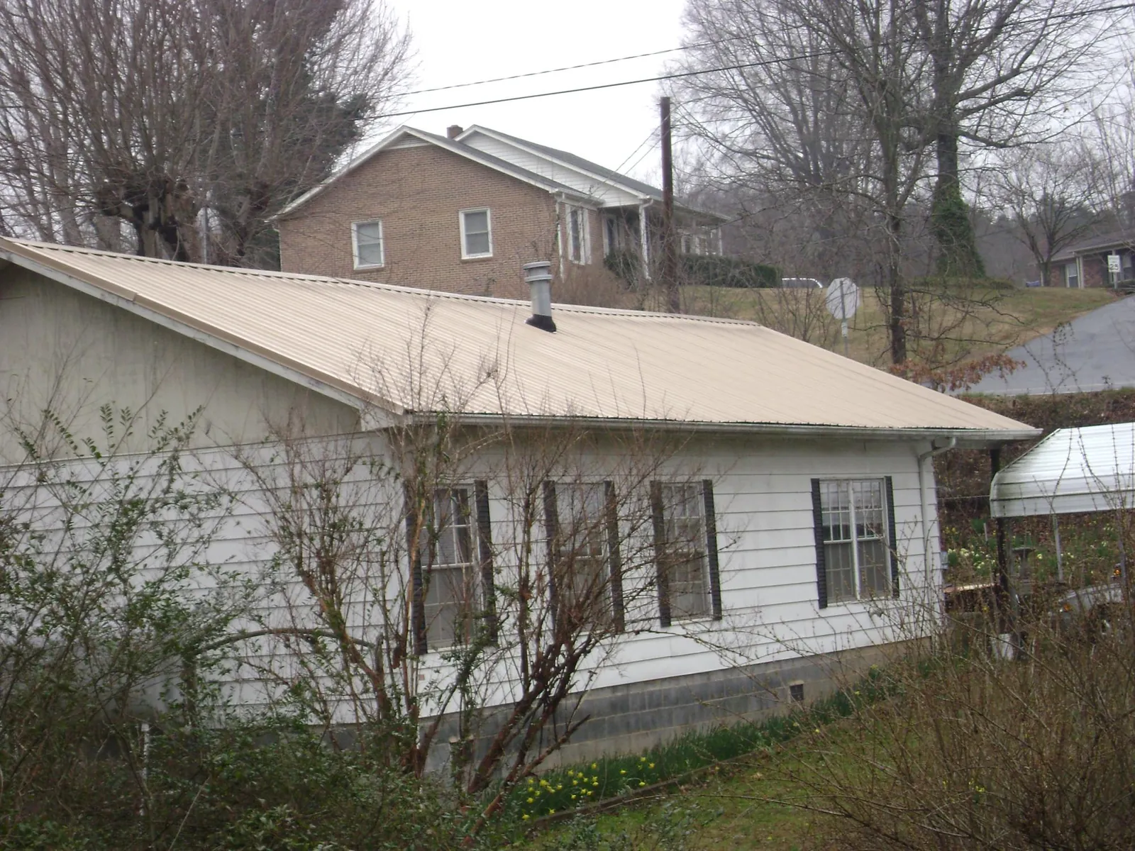 Tan metal roof on a white sided house set into a hillside — Commercial Roofing by Roofing Brothers in Port Hueneme